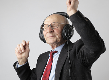 Hymyilevä vanha mies kuulokkeet päässä ja kädet ylhäällä heilumassa musiikin tahtiin